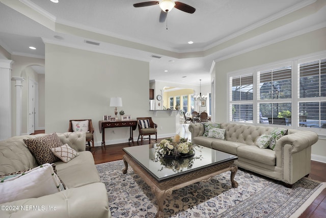 living room with ceiling fan with notable chandelier, dark wood-type flooring, a tray ceiling, and ornamental molding