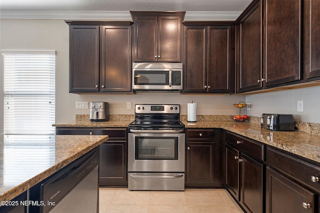 kitchen with appliances with stainless steel finishes, light stone counters, dark brown cabinets, crown molding, and light tile patterned floors