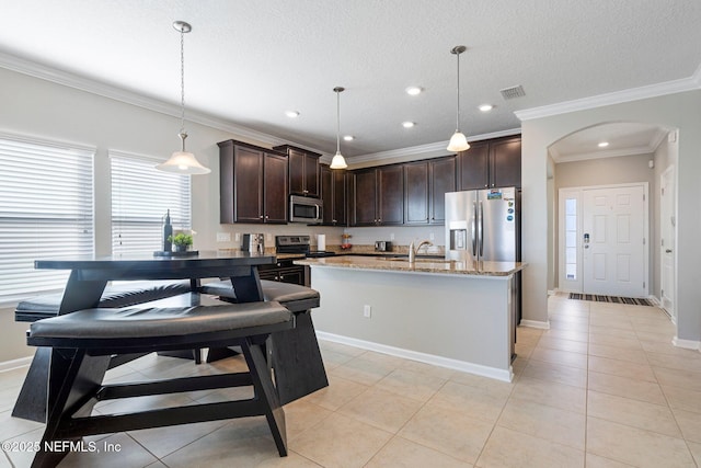 kitchen featuring appliances with stainless steel finishes, light stone counters, a kitchen island with sink, light tile patterned floors, and decorative light fixtures