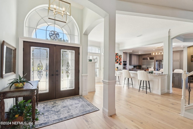 foyer entrance with ornamental molding, french doors, light wood-type flooring, and a notable chandelier