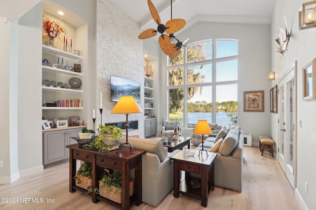 living room with ceiling fan, built in features, high vaulted ceiling, and light wood-type flooring