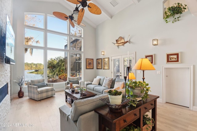 living room featuring a stone fireplace, light hardwood / wood-style flooring, high vaulted ceiling, and beamed ceiling