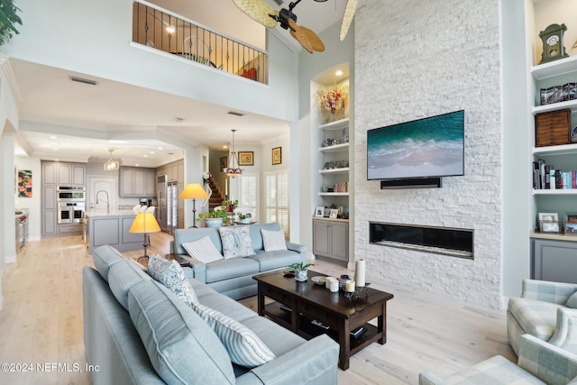 living room featuring ceiling fan, sink, a stone fireplace, built in features, and light hardwood / wood-style flooring