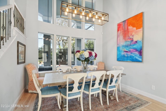 dining space featuring an inviting chandelier, a towering ceiling, and hardwood / wood-style flooring