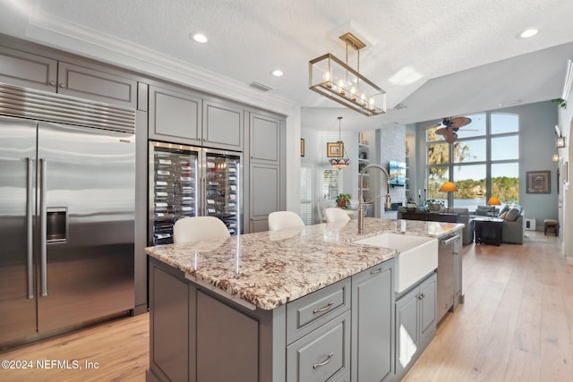 kitchen with a kitchen island with sink, hanging light fixtures, a textured ceiling, stainless steel appliances, and beverage cooler