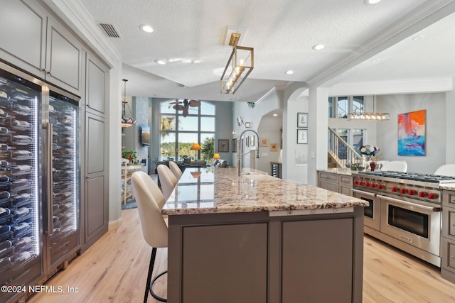 kitchen with ornamental molding, a textured ceiling, a center island with sink, range with two ovens, and gray cabinets