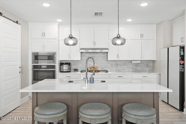 kitchen with appliances with stainless steel finishes, a barn door, pendant lighting, and an island with sink