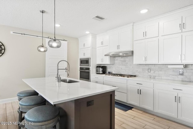 kitchen featuring sink, white cabinetry, hanging light fixtures, a center island with sink, and stainless steel appliances