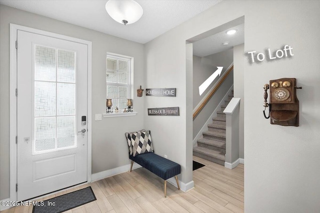 foyer entrance with light wood finished floors, stairway, and plenty of natural light