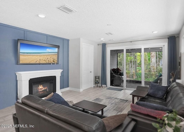 living room featuring light wood-type flooring, visible vents, a textured ceiling, and a glass covered fireplace