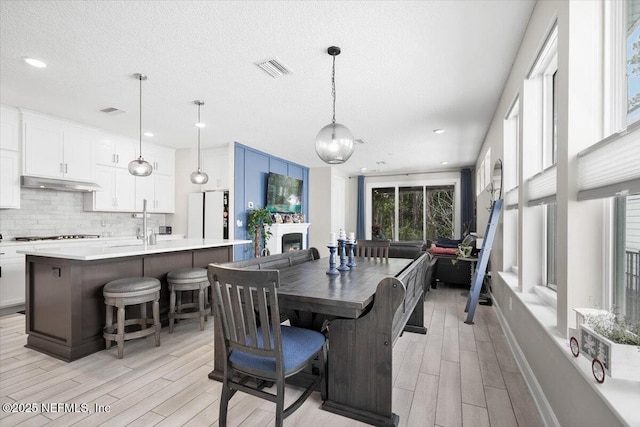 dining space with wood tiled floor, visible vents, a fireplace, and a textured ceiling