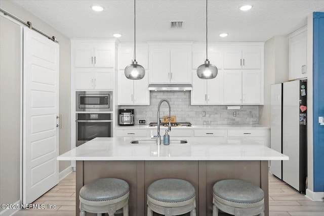 kitchen with stainless steel appliances, visible vents, a barn door, wood tiled floor, and under cabinet range hood