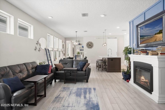 living area with a textured ceiling, a glass covered fireplace, visible vents, and light wood-style floors