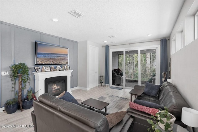 living room with light wood finished floors, visible vents, a textured ceiling, and a glass covered fireplace