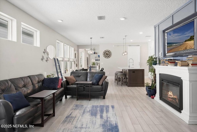 living area with a textured ceiling, visible vents, a glass covered fireplace, and light wood-style flooring