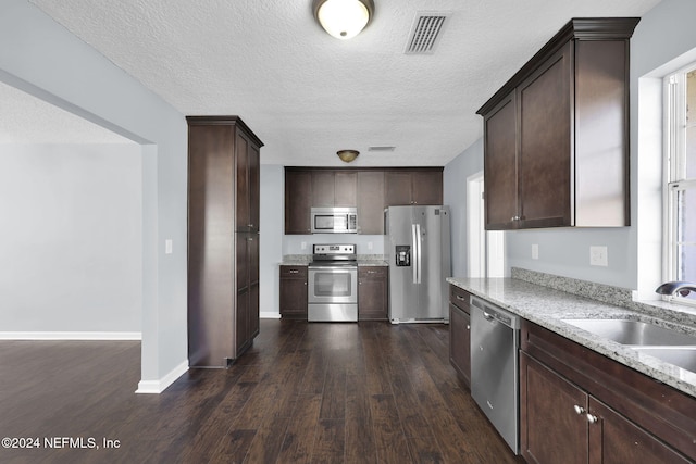 kitchen featuring appliances with stainless steel finishes, dark brown cabinets, sink, dark wood-type flooring, and light stone counters