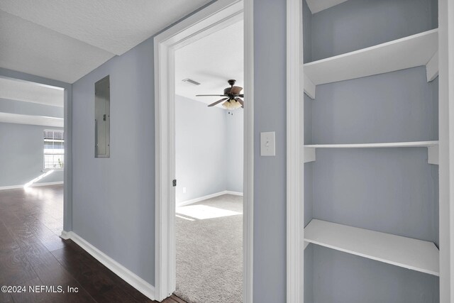 hallway featuring a textured ceiling, electric panel, and dark colored carpet