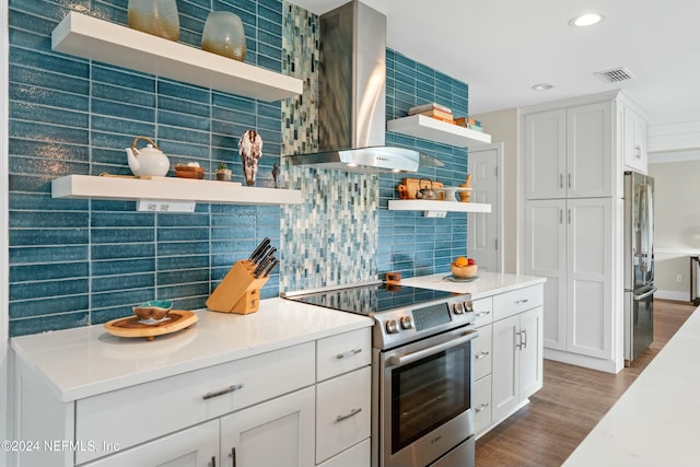 kitchen with hardwood / wood-style flooring, wall chimney exhaust hood, appliances with stainless steel finishes, tasteful backsplash, and white cabinetry