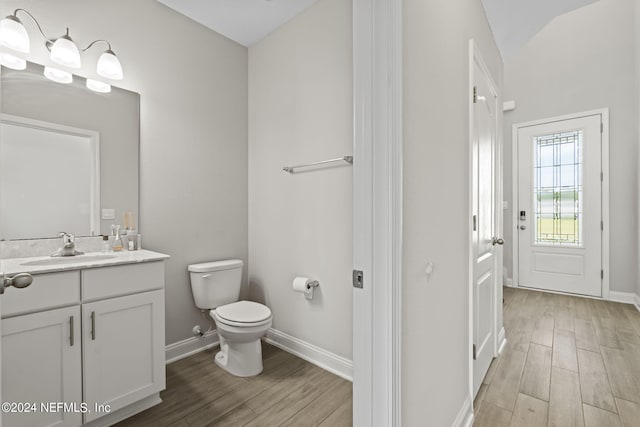 bathroom with hardwood / wood-style flooring, vanity, toilet, and lofted ceiling