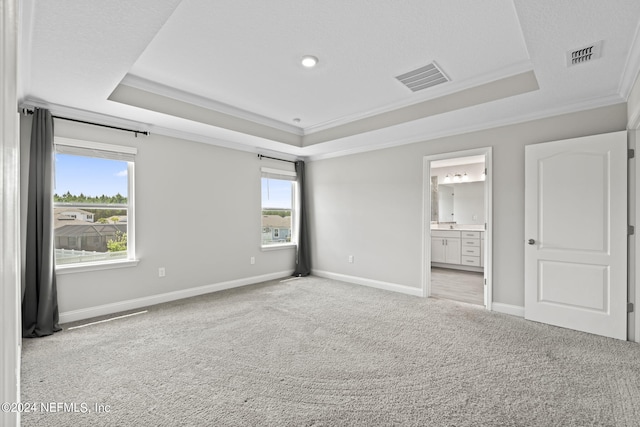 unfurnished bedroom with a tray ceiling, ensuite bath, ornamental molding, and light colored carpet