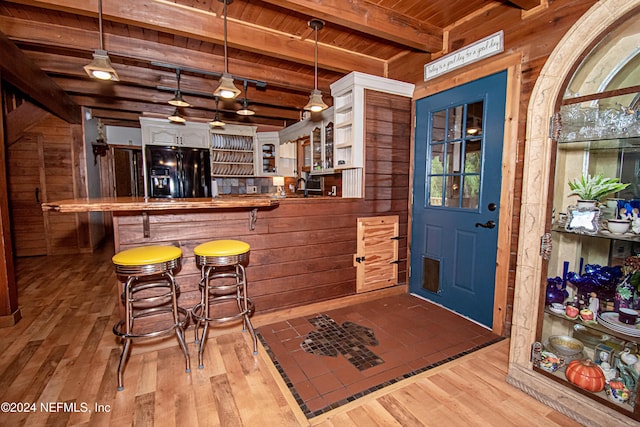 bar featuring black refrigerator with ice dispenser, white cabinets, pendant lighting, and light wood-type flooring