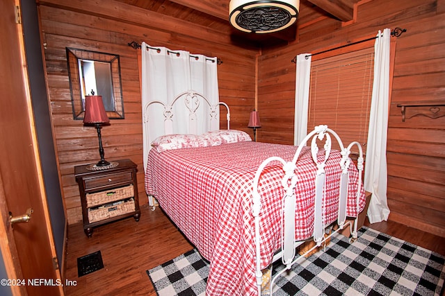 bedroom with beam ceiling, wood walls, and hardwood / wood-style flooring