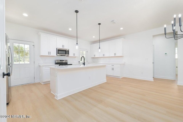 kitchen with a center island with sink, light hardwood / wood-style flooring, decorative light fixtures, white cabinetry, and stainless steel appliances