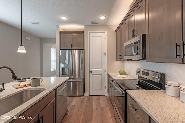 kitchen featuring backsplash, sink, light stone countertops, decorative light fixtures, and stainless steel appliances