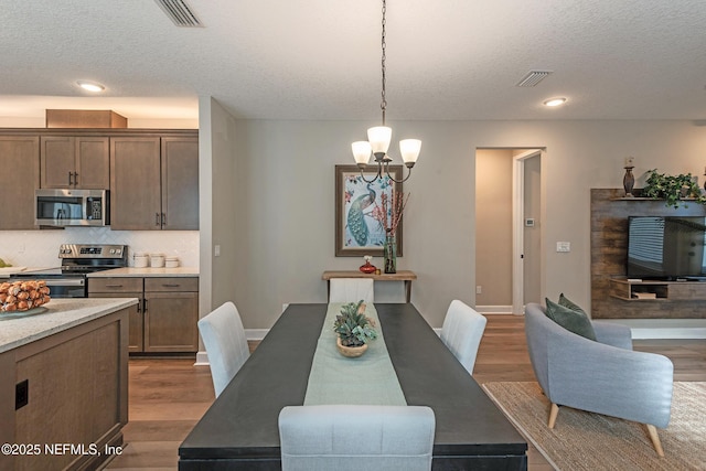 dining area with wood-type flooring, a textured ceiling, and an inviting chandelier