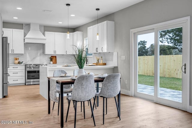 kitchen with premium range hood, appliances with stainless steel finishes, decorative light fixtures, tasteful backsplash, and white cabinetry