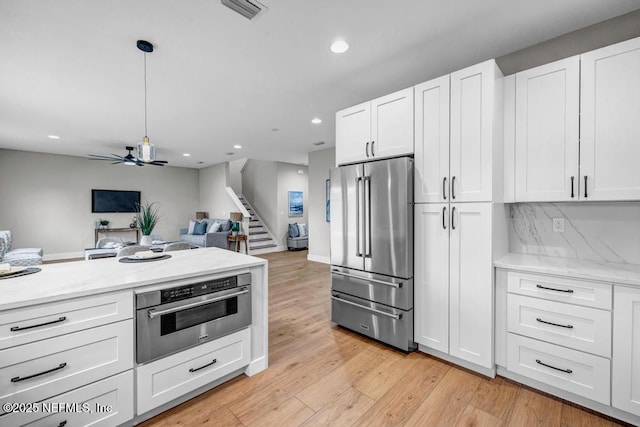 kitchen with white cabinetry, light stone counters, light hardwood / wood-style floors, and appliances with stainless steel finishes