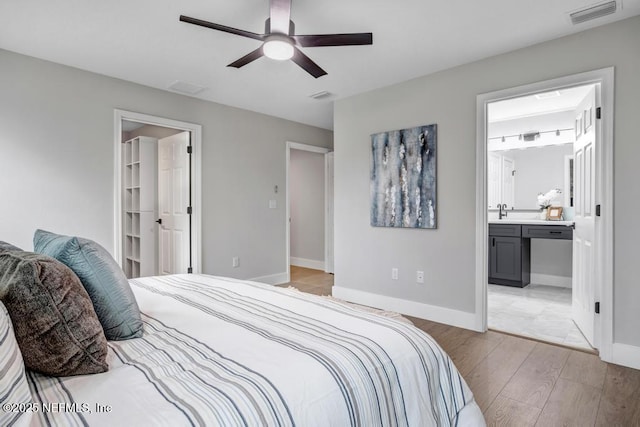 bedroom featuring sink, ceiling fan, ensuite bathroom, light hardwood / wood-style floors, and a spacious closet