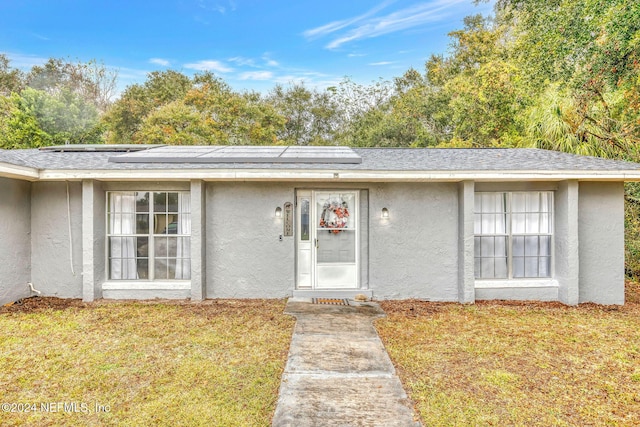 1 Farrington Ln, Palm Coast, FL 32137 - doorway to property with stucco siding, roof mounted solar panels, and a lawn