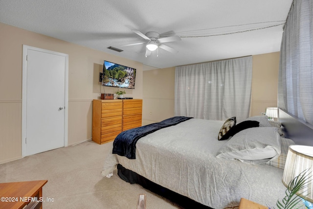 bedroom featuring ceiling fan, light carpet, and a textured ceiling