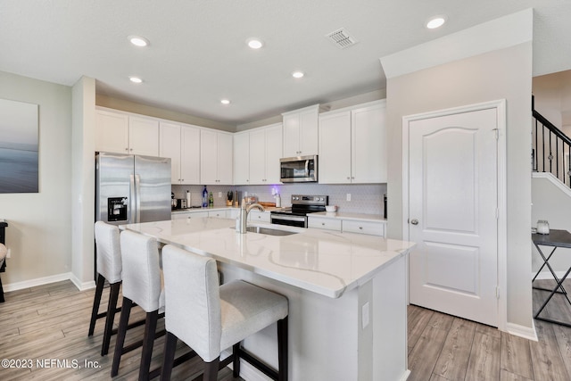 kitchen featuring light hardwood / wood-style flooring, light stone countertops, an island with sink, white cabinetry, and stainless steel appliances