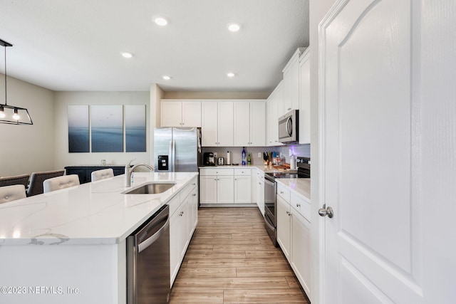 kitchen featuring a kitchen island with sink, white cabinets, decorative light fixtures, and appliances with stainless steel finishes