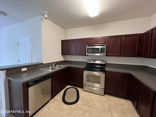 kitchen with a textured ceiling, kitchen peninsula, sink, and appliances with stainless steel finishes