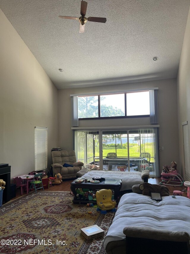 living room featuring ceiling fan, a towering ceiling, a healthy amount of sunlight, and a textured ceiling