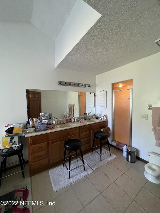 kitchen with a textured ceiling, sink, light tile patterned flooring, and vaulted ceiling