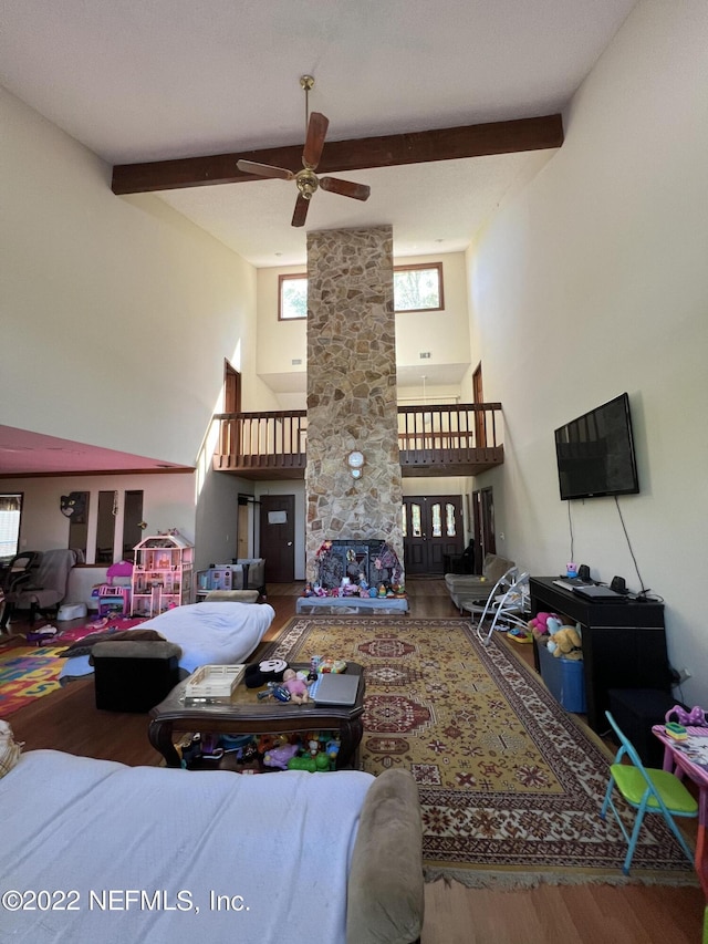 living room with beam ceiling, ceiling fan, a towering ceiling, and wood-type flooring