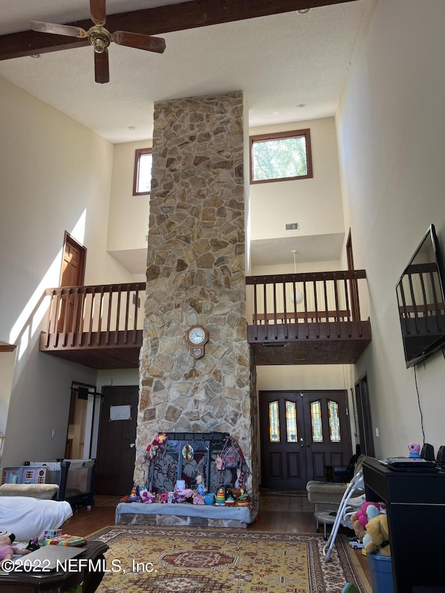 living room with hardwood / wood-style flooring, ceiling fan, a stone fireplace, and a towering ceiling