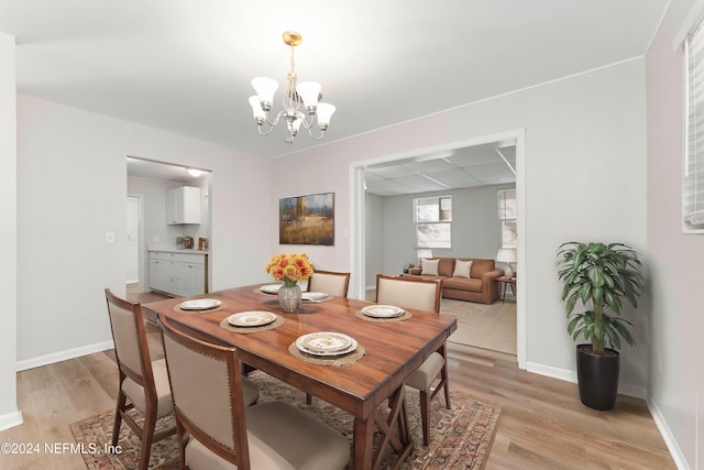 dining space with an inviting chandelier, a drop ceiling, and light wood-type flooring