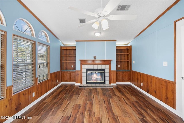 unfurnished living room with a tiled fireplace, dark wood-type flooring, a textured ceiling, and ornamental molding