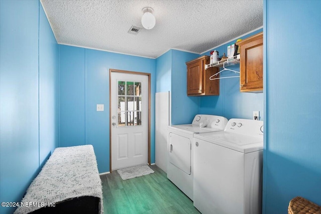 laundry area with washing machine and clothes dryer, cabinets, a textured ceiling, and light wood-type flooring