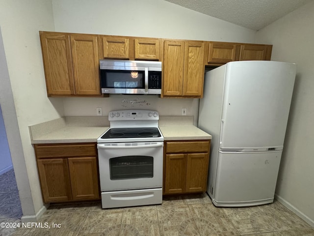 kitchen featuring a textured ceiling, white appliances, light tile patterned floors, and lofted ceiling