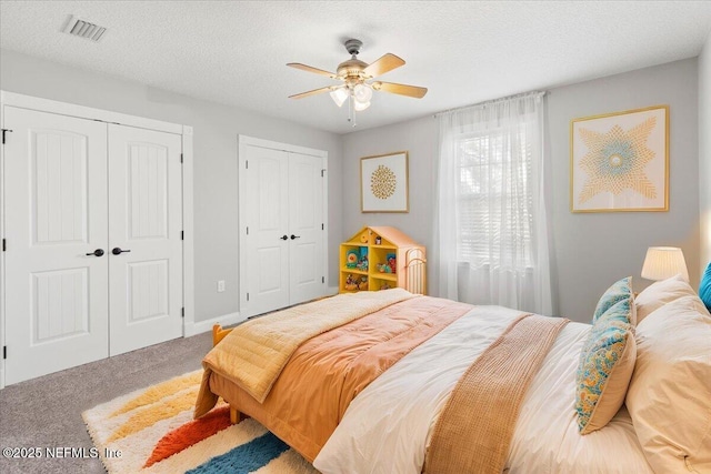 bedroom with a textured ceiling, carpet floors, ceiling fan, and multiple closets