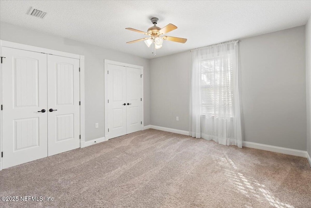 unfurnished bedroom featuring carpet flooring, a textured ceiling, ceiling fan, and multiple closets