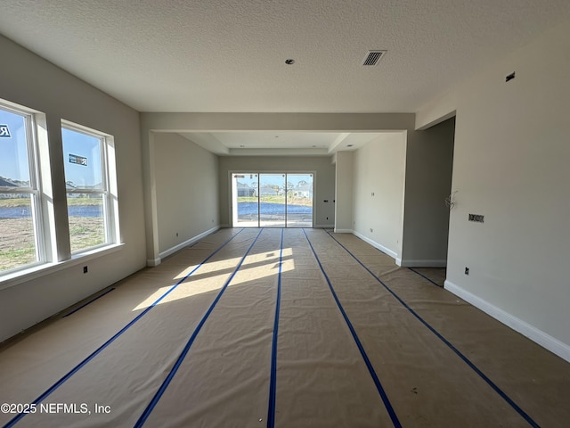 spare room with baseboards, a textured ceiling, visible vents, and a healthy amount of sunlight