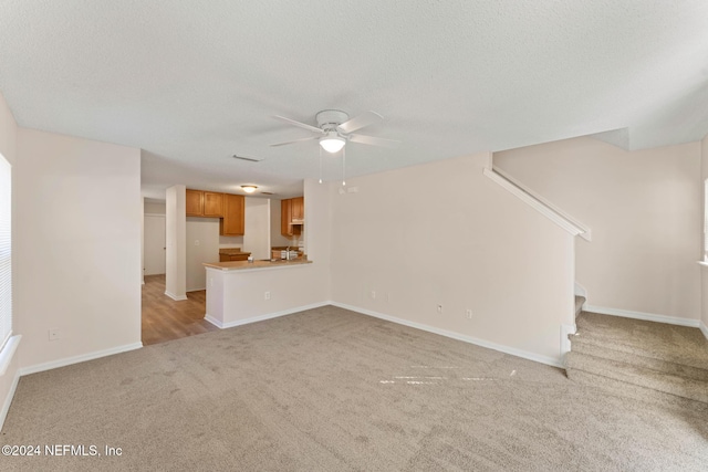 unfurnished living room featuring light carpet, a textured ceiling, and ceiling fan