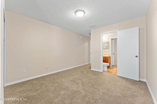 unfurnished bedroom featuring a textured ceiling, light carpet, and ensuite bath